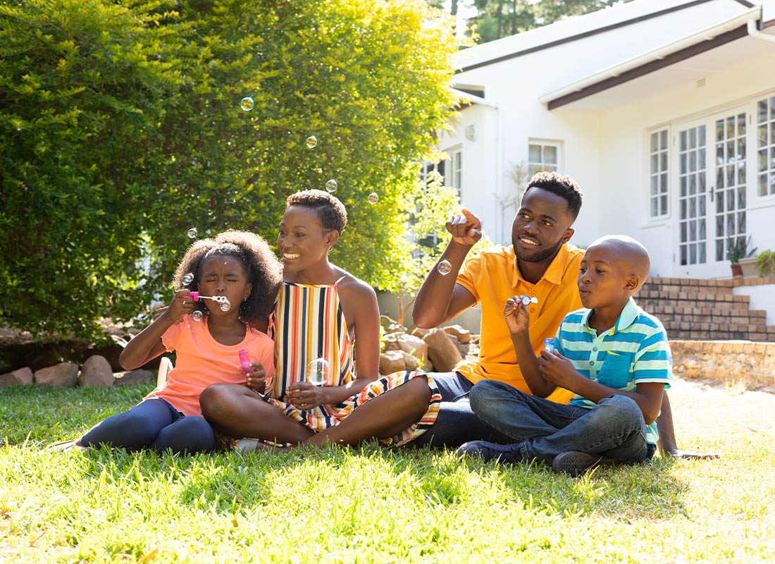 Insurance Solutions - Young Family Having Fun Making Bubbles While Sitting on Their Lawn