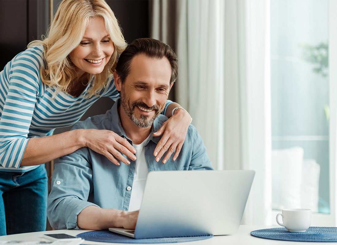 Read Our Reviews - Middle Aged Couple Looking at a Laptop While Smiling at Home